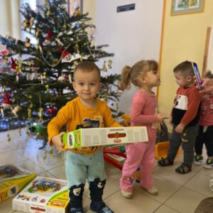 A kar&aacute;csfa k&ouml;r&uuml;l aj&aacute;nd&eacute;kokat bont kisgyermekek.