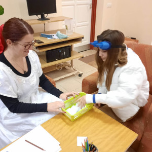 Városi Humánsegítő és Szociális Szolgálat | Galéria Egy hölgy játszik egy fiatal lánnyal egy asztalnál.