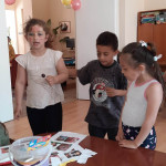 Városi Humánsegítő és Szociális Szolgálat | Galéria Asztal előtt álló gyerekek arcfestéssel.