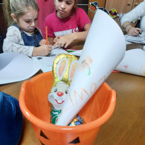 Városi Humánsegítő és Szociális Szolgálat | Halloween a Gyermekjóléti Szolgálatnál Gyerekek rajzolnak egy asztalnál a farsangi bulin, az előtérben egy csokinyuszi.