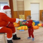 Városi Humánsegítő és Szociális Szolgálat | Mikulás várás a bölcsődében A Mikulás szaloncukrot ad egy kisfiúnak.