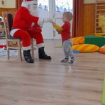 Városi Humánsegítő és Szociális Szolgálat | Mikulás várás a bölcsődében A Mikulás szaloncukrot ad egy kisfiúnak.
