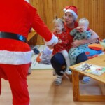 Városi Humánsegítő és Szociális Szolgálat | Mikulás várás a bölcsődében A Mikulás szaloncukrot ad egy kislánynak.