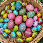 Egy színes, kézzel díszített és becsomagolt húsvéti tojásokkal teli kosár, amely változatos mintákat és vidám mintákat mutat be, egy zöld füves ágy tetején.