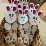 Aranyos nyuszi témájú kézműves dekorációkkal teli kosár csokoládétáblákhoz rögzítve, ünnepi húsvéti csemege bemutatót teremtve.