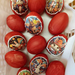 Élénk pirosra festett húsvéti tojások gyűjteménye ünnepi matricákkal díszítve, amelyeken különböző játékos és kalandos jelenetekben rajzfilmes nyulak láthatók.