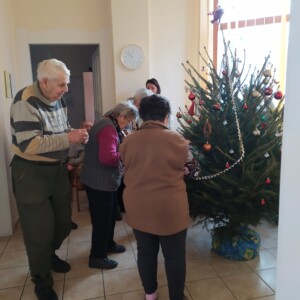 Városi Humánsegítő és Szociális Szolgálat | Galéria Idősek csoportképe egy Karácsonyfa mellett.