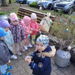 Kisgyermekek egy csoportja, akik szabadtéri húsvéti tojásvadászatot élveznek, és az egyik gyermek büszkén mutogatja a színes tojást.
