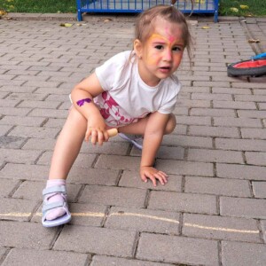 Városi Humánsegítő és Szociális Szolgálat | Gyermeknap a bölcsődében Egy krétával a földre rajzoló kislány.