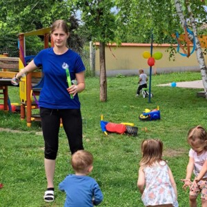 Városi Humánsegítő és Szociális Szolgálat | Gyermeknap a bölcsődében A kisgyermeknevelő buborékokat fúj a körülötte álló gyermekeknek.