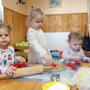 3 kislány játszik egy fa asztalon konyhai eszközökkel.