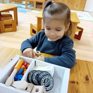 Egy kisl&aacute;ny űl egy asztaln&aacute;l amelyben szersz&aacute;m j&aacute;t&eacute;kok vannak